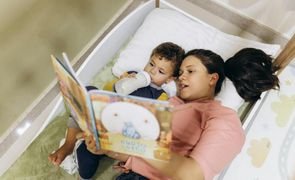 mulher   segurando livro deitada com bebe que esta segurando uma mamadeira