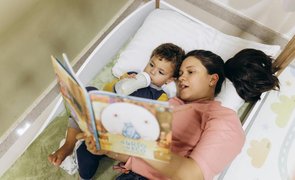 mulher   segurando livro deitada com bebe que esta segurando uma mamadeira