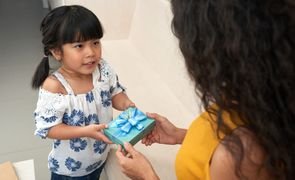 crianca asiatica recebendo presente de mulher do qual esta de costas para foto