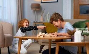 dois meninos sentados no chao perto de mesa central dando risada com pecas de jogo sobre a mesa dois meninos sentados no chao perto de mesa central dando risada com pecas de jogo sobre a mesa