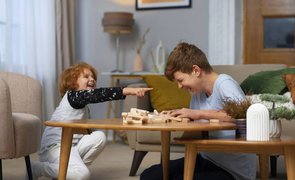 dois meninos sentados no chao perto de mesa central dando risada com pecas de jogo sobre a mesa