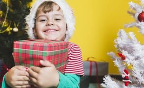 menino com gorro de natal abracando um presente com arvores de natal ao fundo