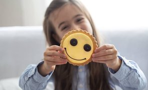 menina segura um biscoito sorridente amarelo sobre um fundo desfocado