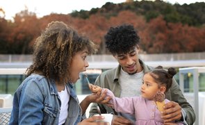 mae pai e filha ao ar livre com menininha levando colher com sorvete pra mae